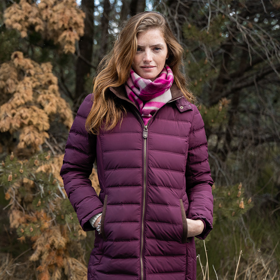 Woman wearing a purple puffer coat and pink scarf standing in a forest.