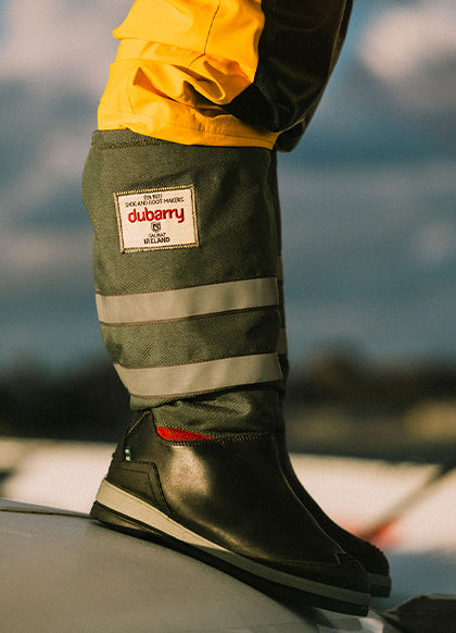 Person wearing green work pants with a Dubarry label and black boots, standing on a vehicle.