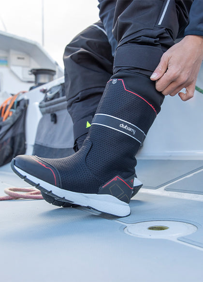Person wearing black rubber boots with red accents on a boat deck.