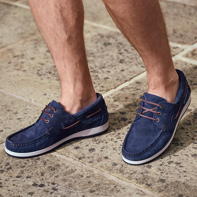 Navy blue Dubarry suede shoes with white soles on a stone pavement