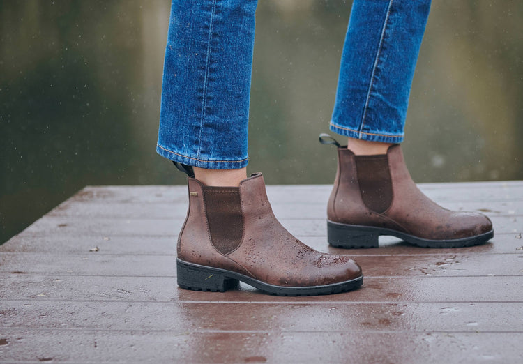 On model image of a woman wearing a pair of Dubarry Waterford old rum coloured leather country boots, women's Chelsea style boot with Elasticated side gussets and heel finger pull on a lake pier.