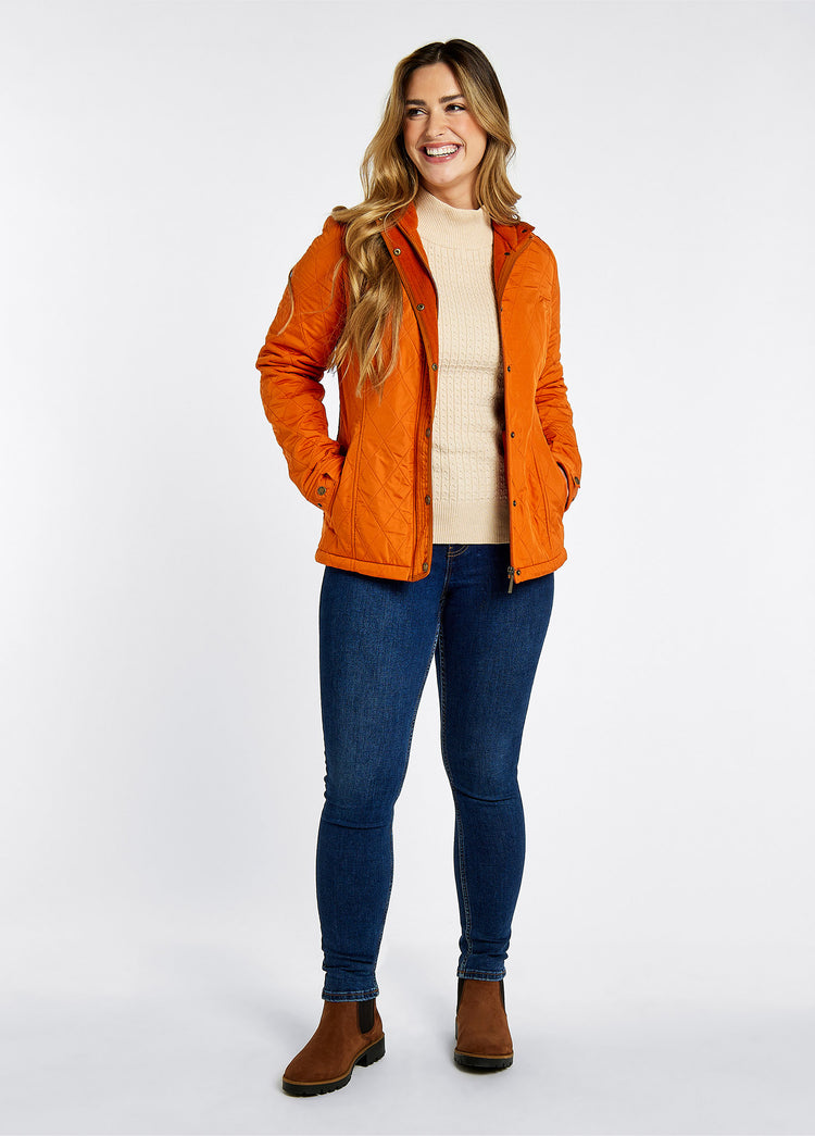 On model image of a woman wearing a Pair of Dubarry Waterford walnut coloured leather country boots,  women's Chelsea style boot with Elasticated side gussets and heel finger pull. She is also wearing an orange wax jacket, cream knitted jumper and a denim pair of honeysuckle jeans.