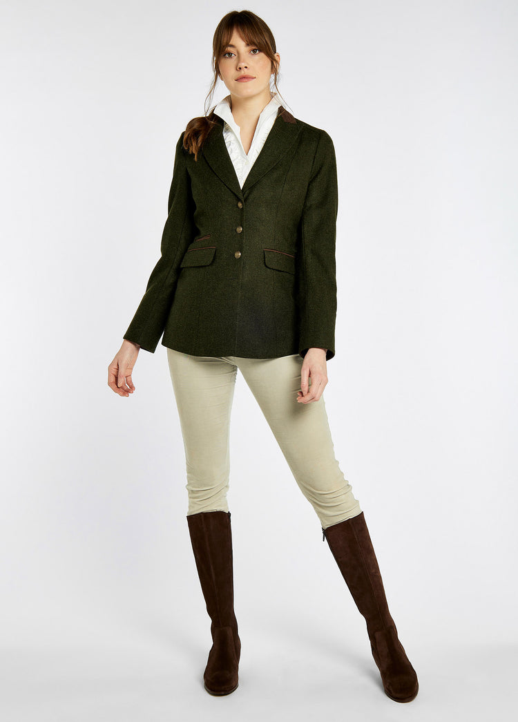 A woman modelling Dubarry women's Rockberry Tweed loden Blazer with brass buttons and stripe sleeves. She is also wearing a white shirt, white honeysuckle jeans and brown boots.