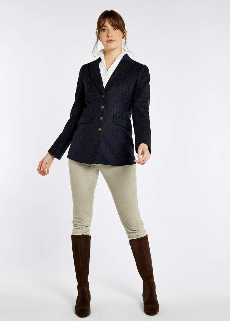 A woman modelling Dubarry women's Rockberry Tweed Navy Blazer with brass buttons and stripe sleeves. She is also wearing a white shirt, white honeysuckle jeans and brown boots.