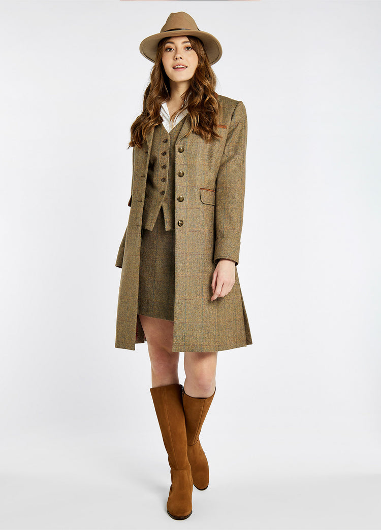 On Model image of a woman wearing a pair of Ladies Dubarry knee-high Camel Downpatrick Country Boot with Full length zip fastening. She is also wearing an open tweed coat with matching waist coat and skirt. She is also wearing a white shirt and a brown hat.