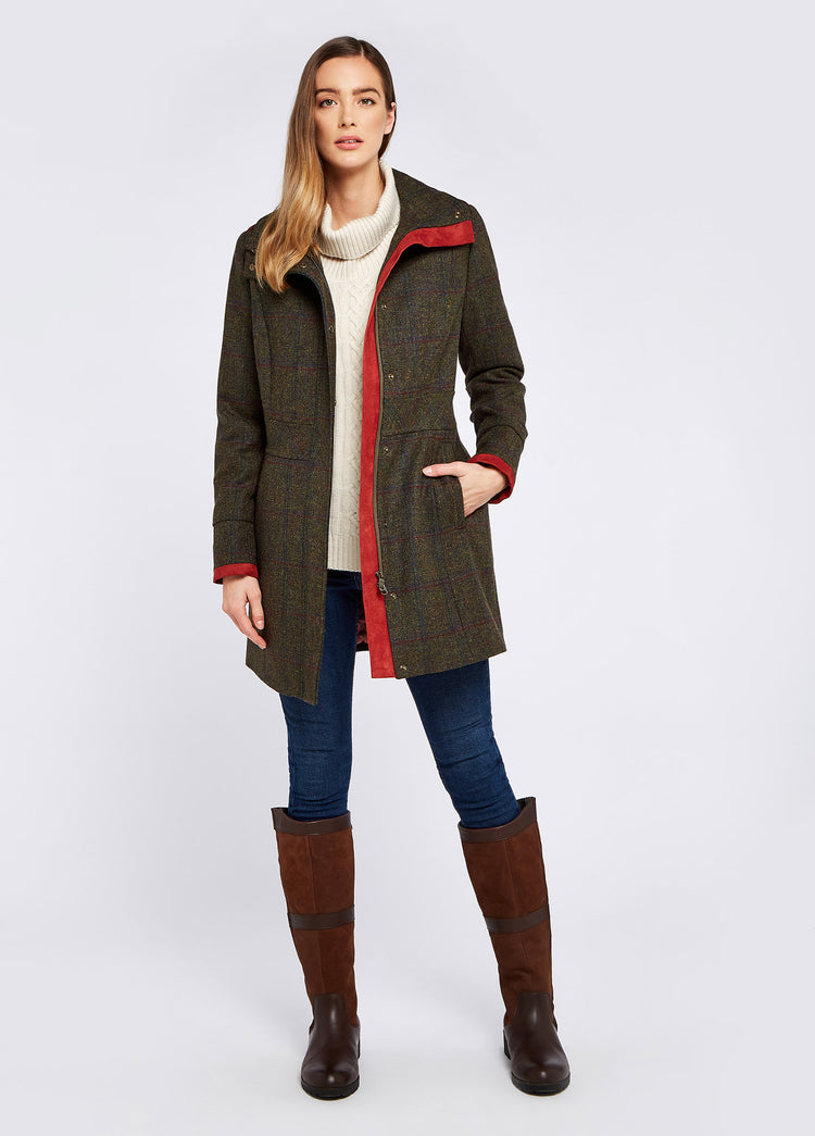 "A woman modelling Dubarry women's Hedgerow Tweed Hemlock Coat with a two-way, centre front zip, vertical pockets and high-collar. She is also wearing blue jeans and brown boots.
"