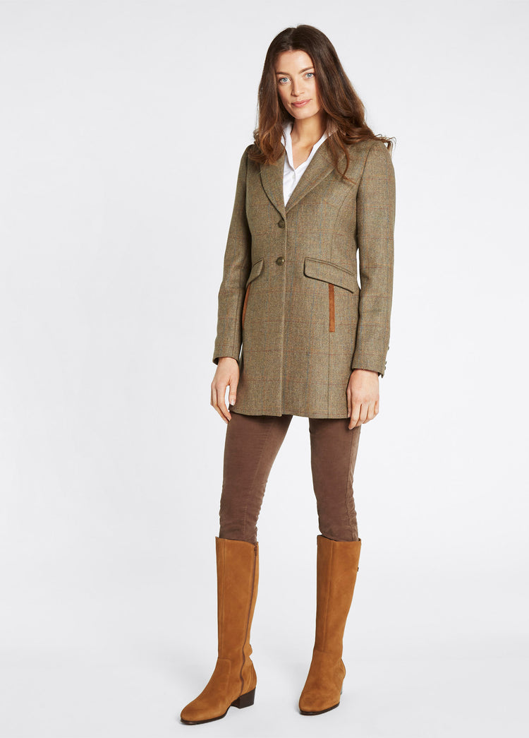 On model image of a female model wearing Dubarry women's Treefern Tweed burren jacket with smart button fastenings and pockets are trimmed with suede. She is also wearing a white shirt, brown honeysuckle jeans and tan knee-high boots. 