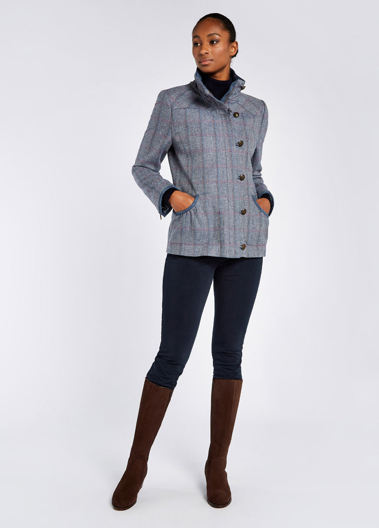 A woman modelling Dubarry women's Bracken Tweed Denim Haze Jacket with cast metal buttons and full-lenght zip which extends to the stand-up collar. She is also wearing navy honeysuckle jeans and brown boots.