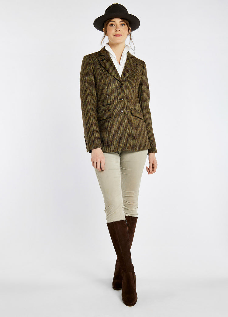 A woman modelling Dubarry women's Darkhedge Tweed Heath Jacket with stripe sleeve lining, buttons and single back vent. The model is also wearing a hat, white honeysuckle jeans and brown boots.