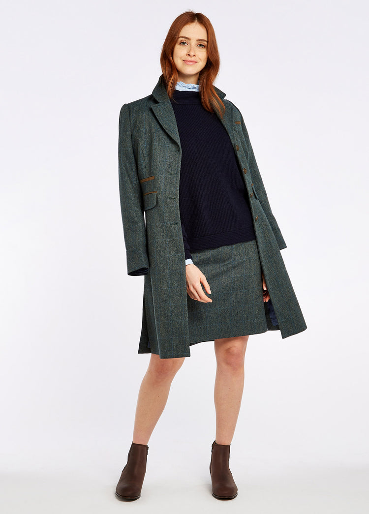 A woman modelling Dubarry women's Blackthorn Tweed Mist Coat draped over her shoulders unbuttoned. Model is also wearing a navy jumper, skirt and boots.