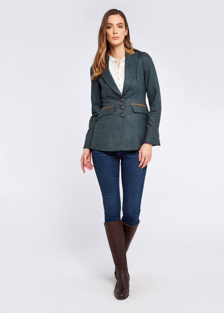 A woman modelling Dubarry women's Heather Tweed Mist Coat with stripe sleeves and metal buttons. She is also wearing a white shirt, blue jeans and brown boots.