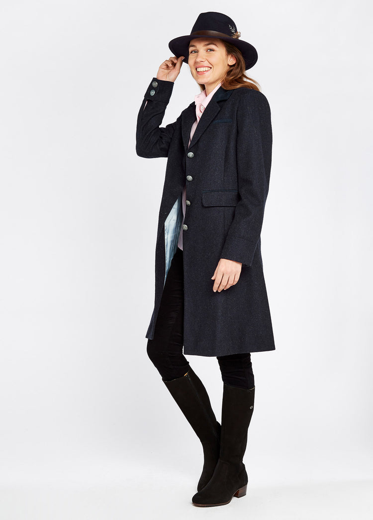 Woman modelling Dubarry Blackthorn Navy Tweed Coat, three-quarter-length tailored jacket with besom pockets. The woman is standing at an angle with the jacket open and is wearing a hat, top, jeans and boots. 