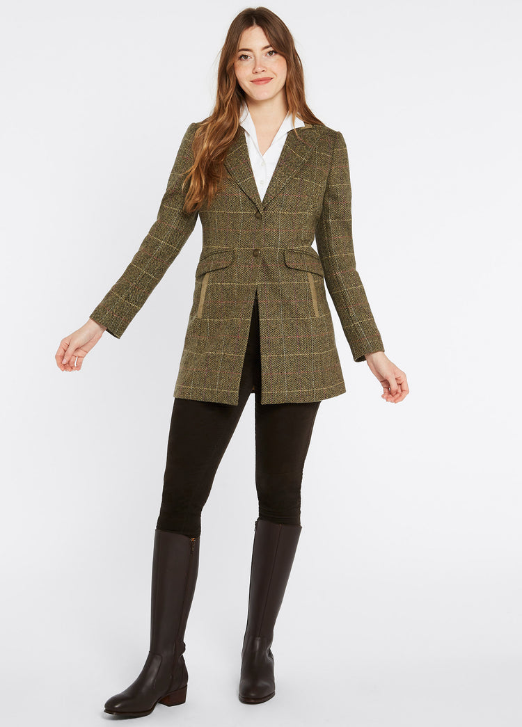 On model image of a female model wearing Dubarry women's Treefern Tweed thistle jacket with smart button fastenings and pockets are trimmed with suede. She is also wearing a white shirt, black honeysuckle jeans and brown knee-high boots. 