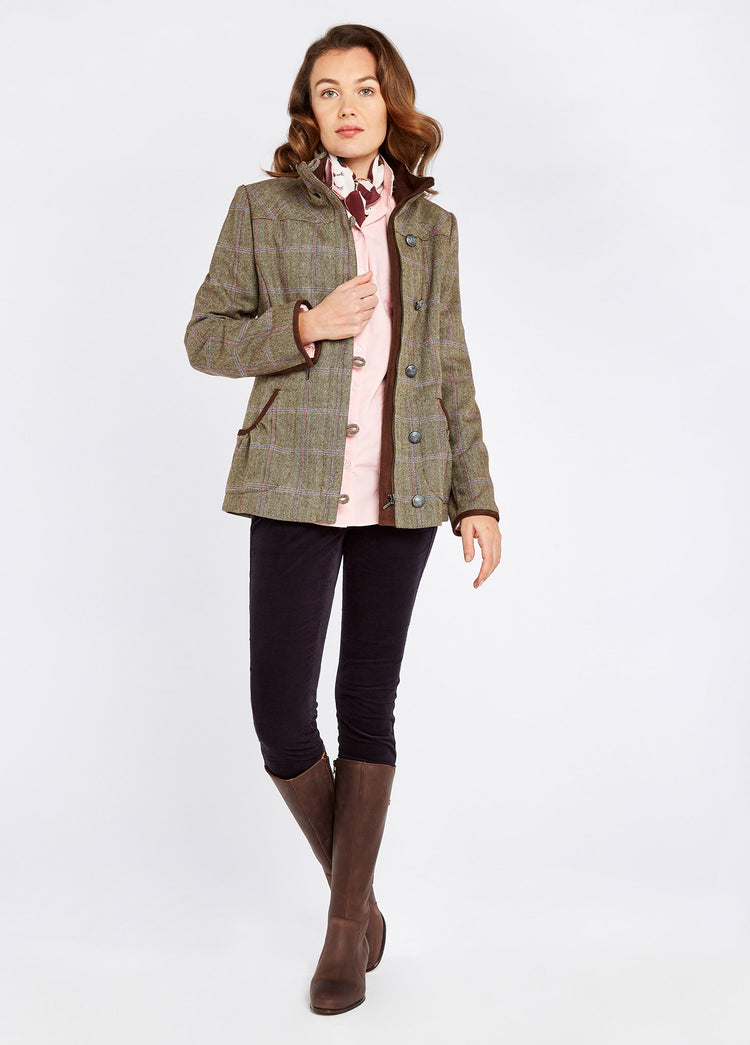A woman modelling an unzipped Dubarry women's Bracken Tweed  Woodrose Coat with metal buttons and high collar. She is also wearing a pink shirt, black pants and brown boots.