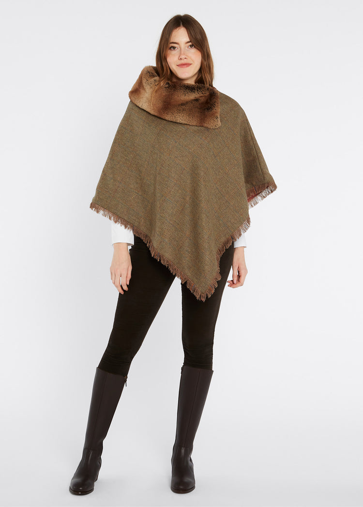 On model image of Dubarry women's Silverfir Tweed burren Poncho, coated with 100% pure wool. She is also wearing black honeysuckle jeans and brown knee-high boots.