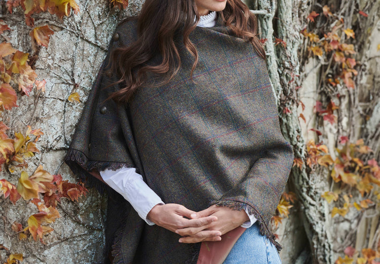 Woman modelling Hazelwood Tweed Hemlock Poncho from an angle with functional button detail on one side and fabric fringe. 