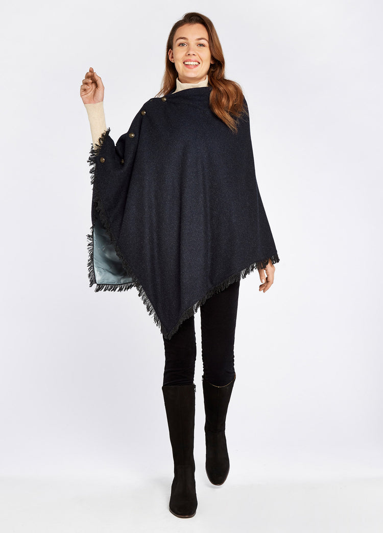 Woman modelling Hazelwood Tweed Navy Poncho with functional button detail on one side and fabric fringe. She is also wearing navy honeysuckle jeans and dark coloured boots