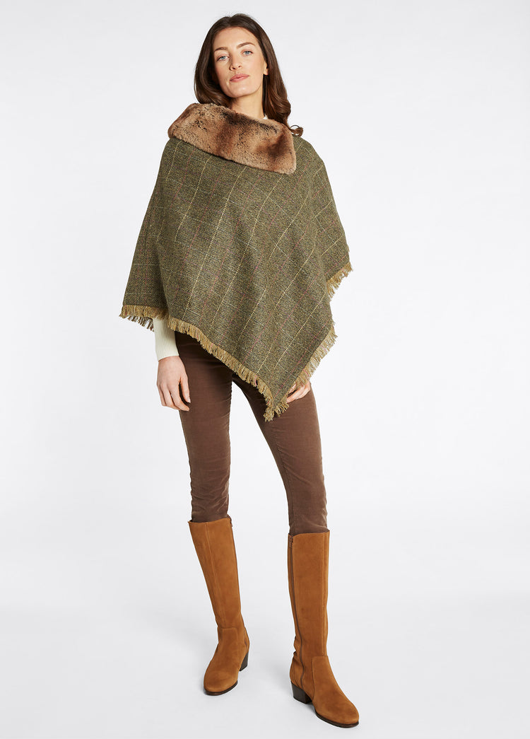 On model image of Dubarry women's Silverfir Tweed thistle Poncho, coated with 100% pure wool. She is also wearingbrown honeysuckle jeans and tan knee-high boots.