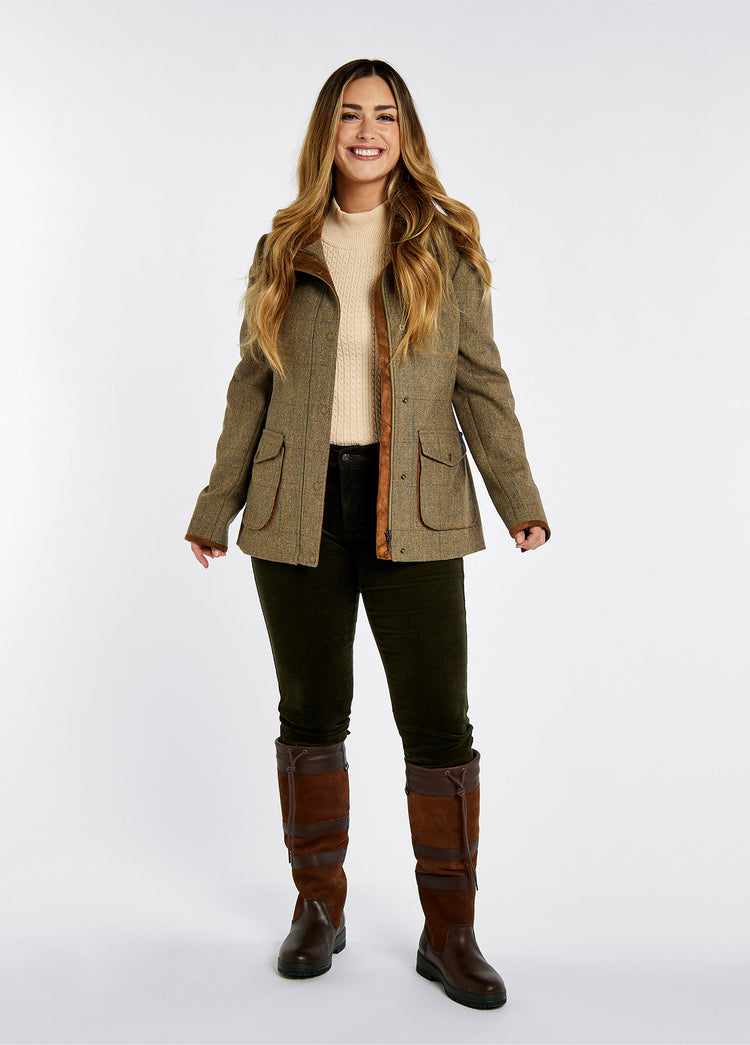 A woman modelling Dubarry women's Betony Tweed Burren Jacket with sleeve lining, lined collar and cargo pockets. She is also wearing green honeysuckle jeans and brown boots.