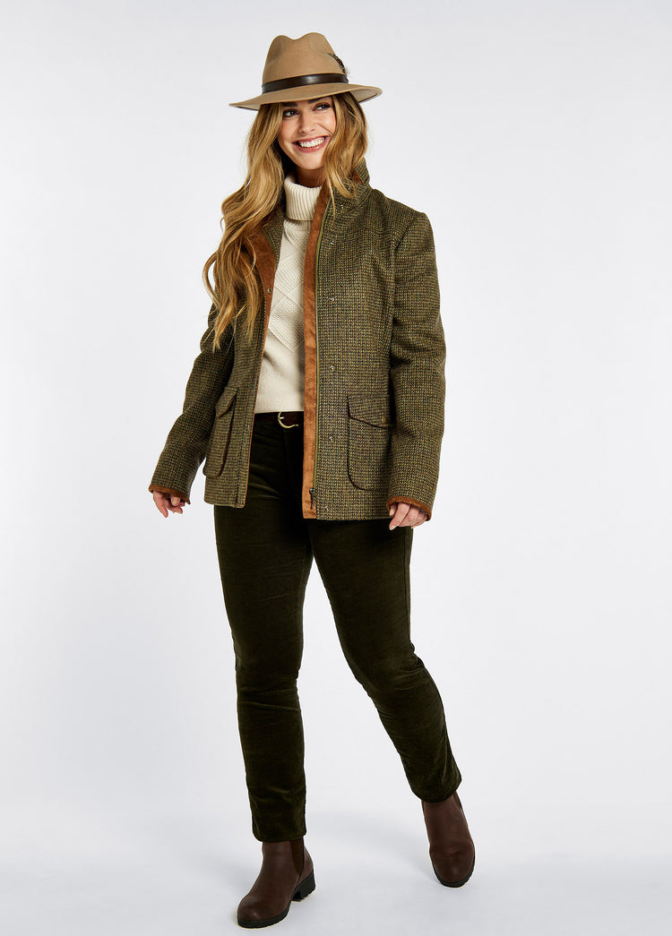 A woman modelling Dubarry women's Betony Tweed heath Jacket with sleeve lining, lined collar and cargo pockets. She is also wearing a cream knitted jumper, green honeysuckle jeans and brown boots.