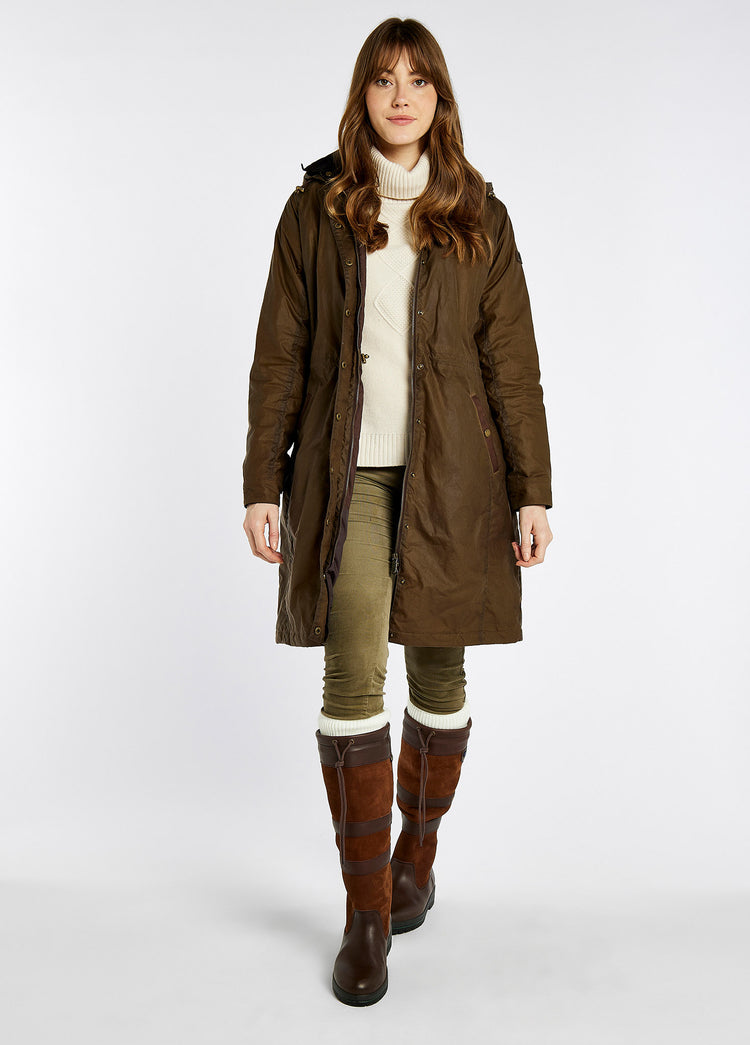 A female model wearing a ginger brown Dubarry Redington Wax coat, longer length coat with  full zip. Model is wearing a light coloured jumper underneath. 