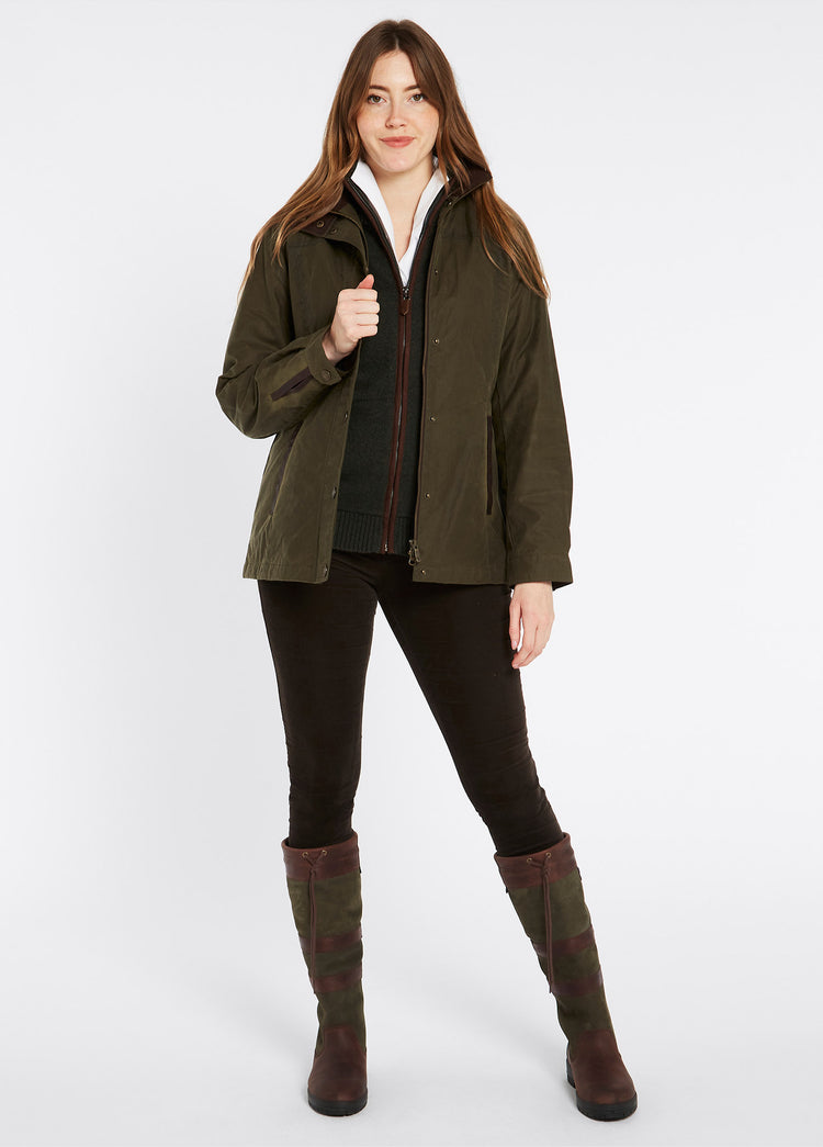 A female model wearing an opened Dubarry Mountrath Waxed fennel coloured jacket with full zip and buttons, brown edged pockets, inner collar and brown inside collar. The model is also wearing a dark top underneath, dark jeans and brown boots