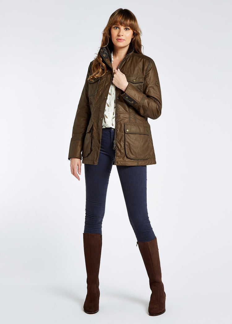 A female model wearing a ginger brown Dubarry Munsboro wax jacket, high collared jacket with golden buttons, pockets and full zip