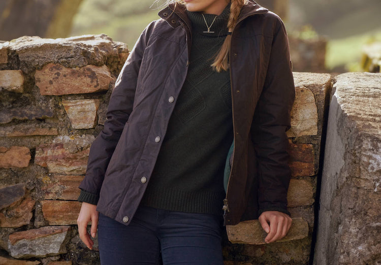 Waist up view of a female model wearing a Dubarry Mountrath java brown coloured waxed jacket opened, with full zip and buttons. The model is also wearing a dark shirt