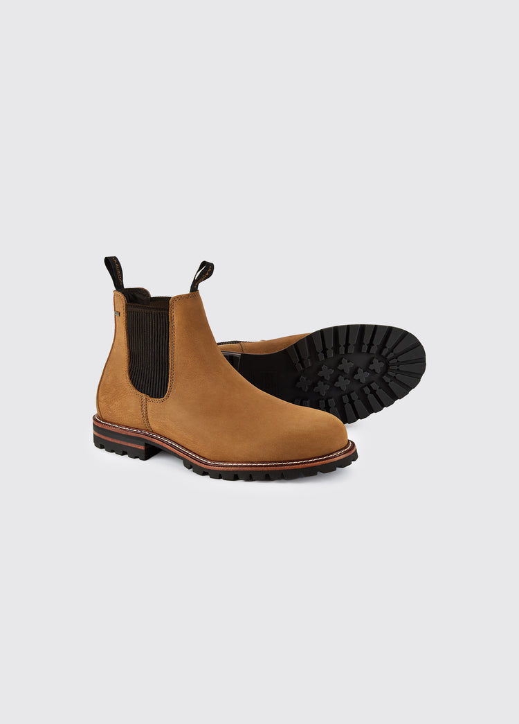 A pair of Dubarry Offaly ankle boots, brown men's seude look cleated chelsea boots with elasticated side gussets and leather finger pulls. One boot's sole is on display