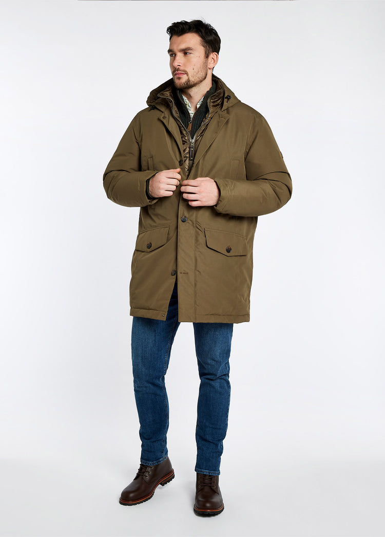 On model image of a man wearing A pair of Dubarry Laois boot, mahogany brown men's laced leather ankle boots with ski hooks and heel finger pull. He is also wearing a brow quilted jacket and blue denim jeans.