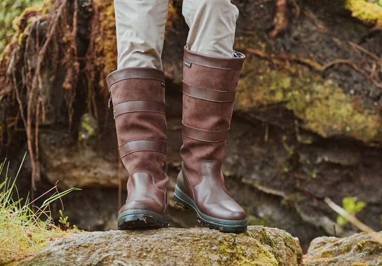 On model image of a man wearing a pair of Dubarry mens wider fitting Wexford country leather boots with side zip, java brown colour in a grassland area. 