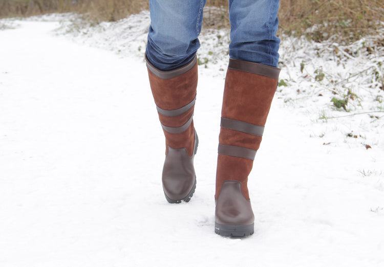 On model image of a man wearing a pair of full length Dubarry mens Kilternan Country Boots, walnut coloured ski style leather boot standing in the snow.