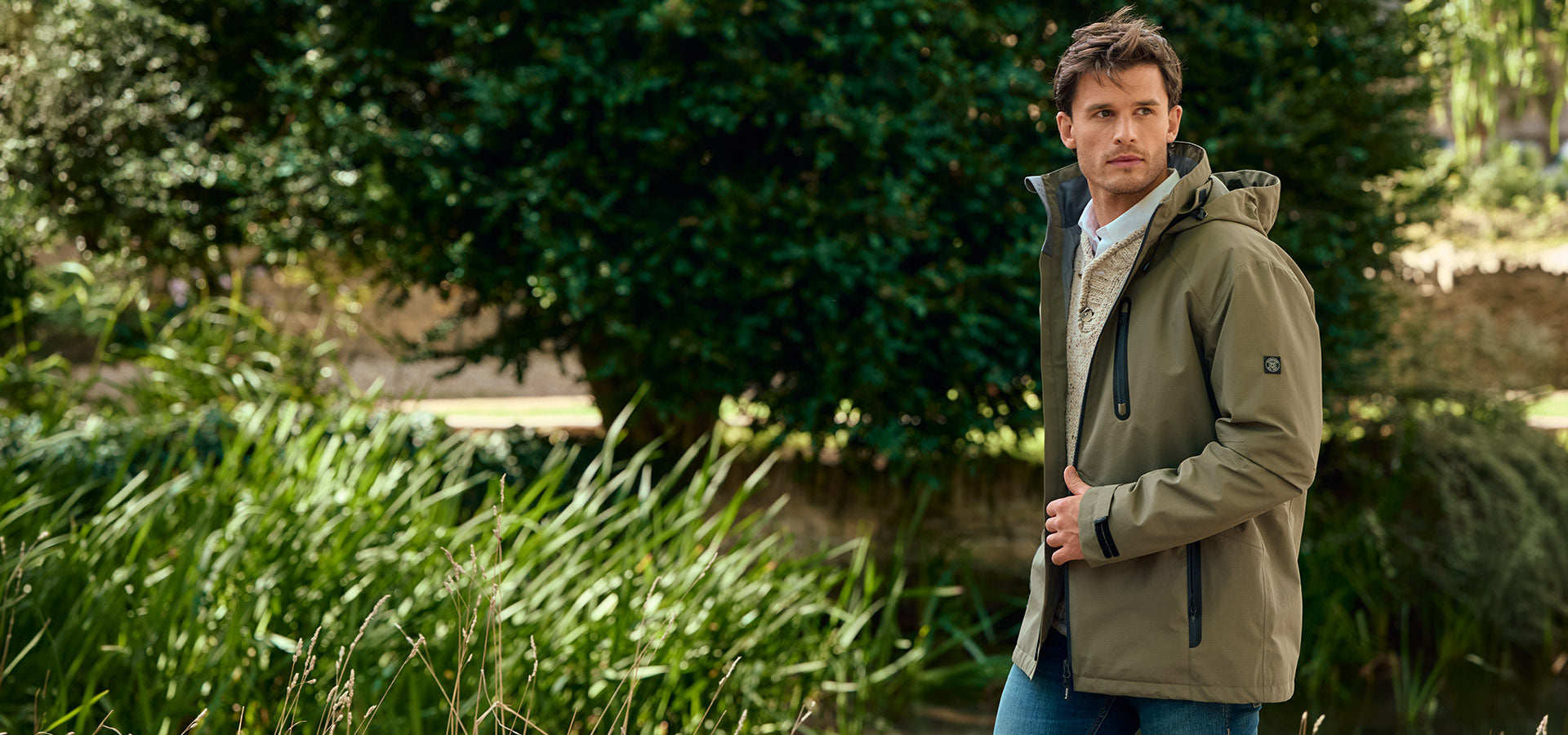 Man wearing a Dubarry green jacket standing outdoors with greenery in the background