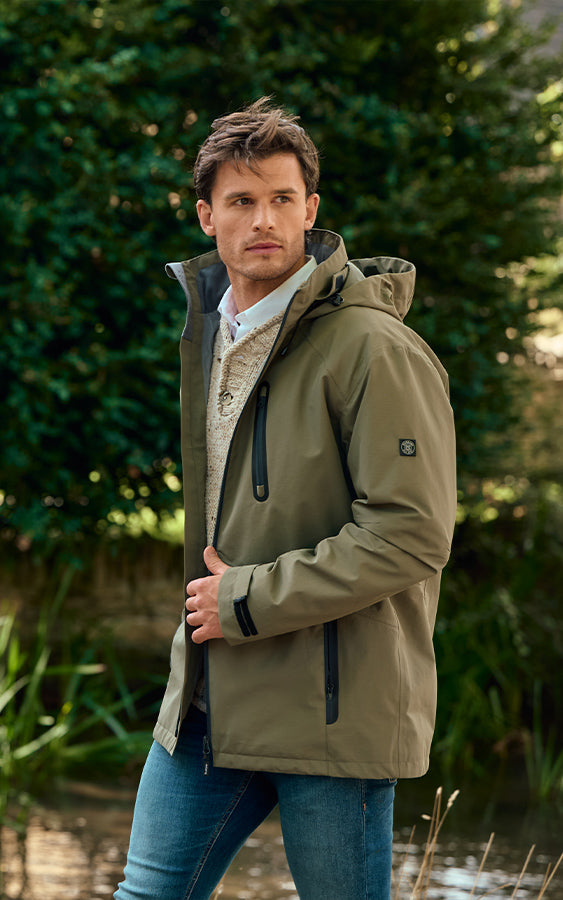 Man wearing a Dubarry green jacket standing outdoors with greenery in the background