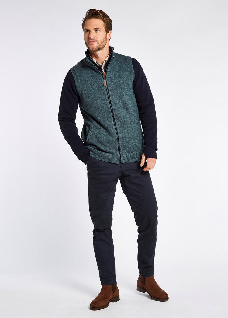 An on model image of a man wearing a pair of Dubarry Kerry Chelsea boots for men, cigar brown coloured leather with elasticated side gussets with front and heel finger pulls, navy zip up fleece, and navy trousers. 