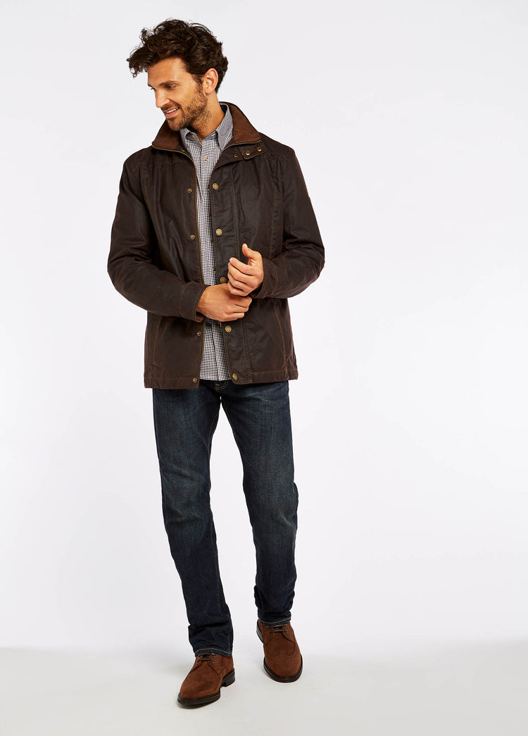 Waist up view of a male model wearing a java brown coloured Dubarry Carrickfergus waxed jacket, open with the lighter brown inside collar visible. The model is also wearing a white and black checkered shirt