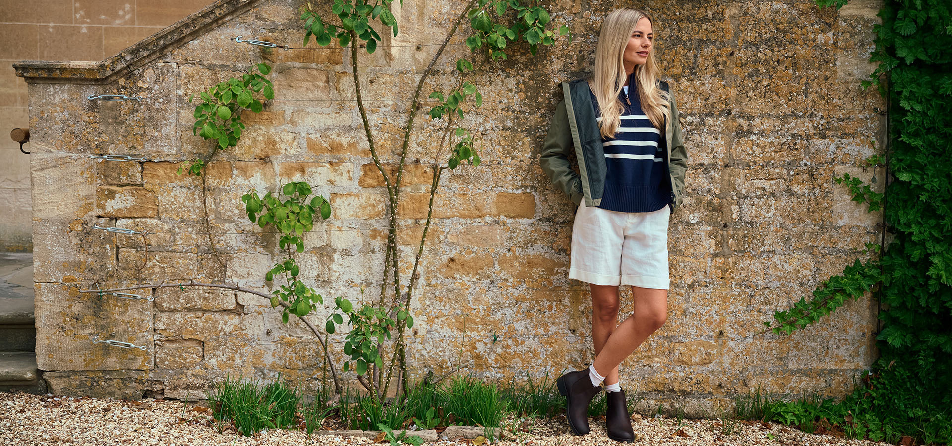 Woman standing against a stone wall with greenery