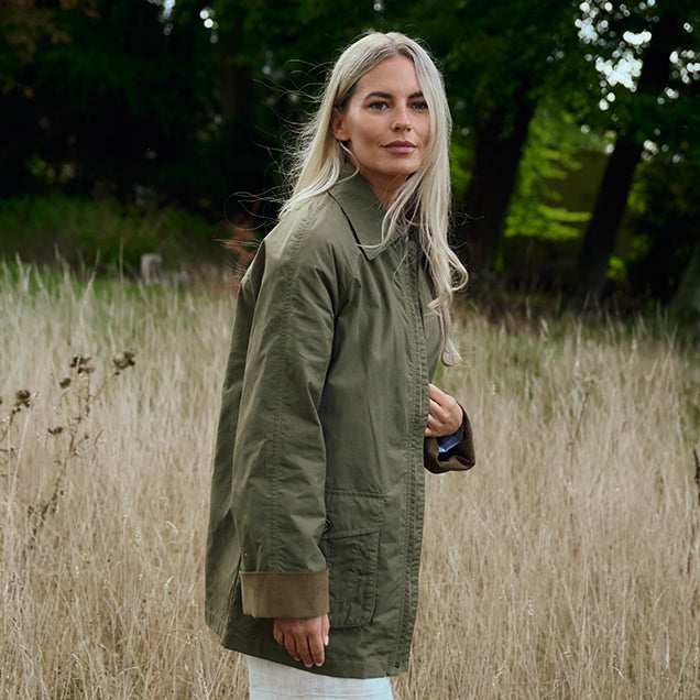 Woman wearing a Dubarry green jacket standing in a field with trees in the background